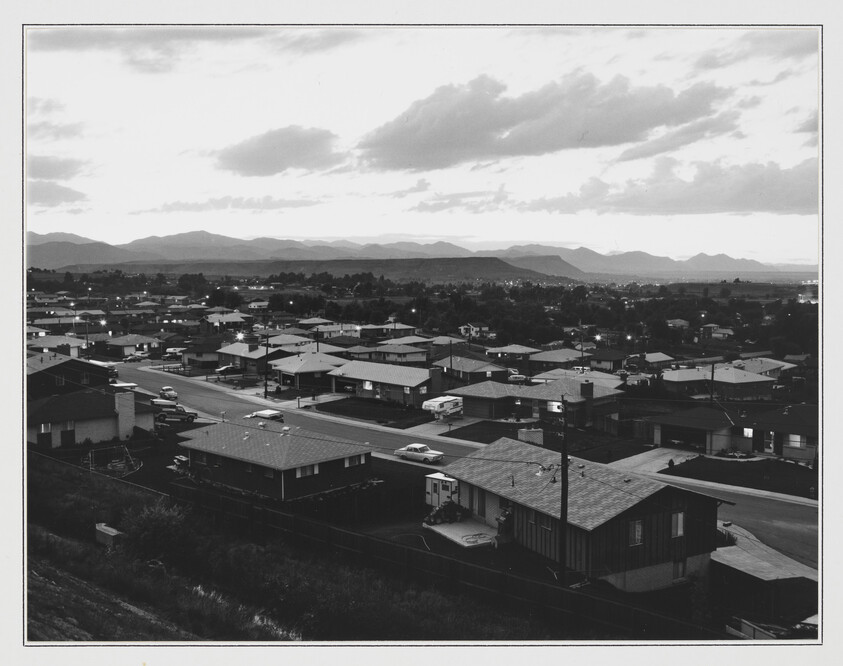 A quiet suburban neighborhood at dusk with rows of single-story houses and distant mountains.