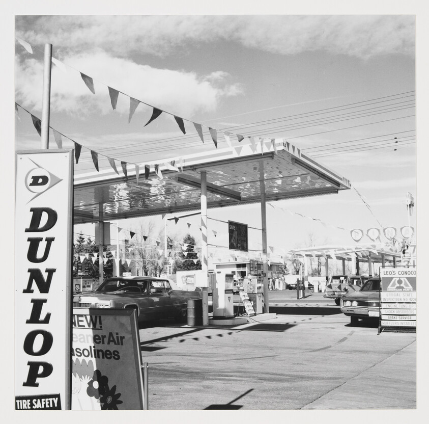 A vintage gas station with pennant flags, pumps, and a large Dunlop sign in the forefront.