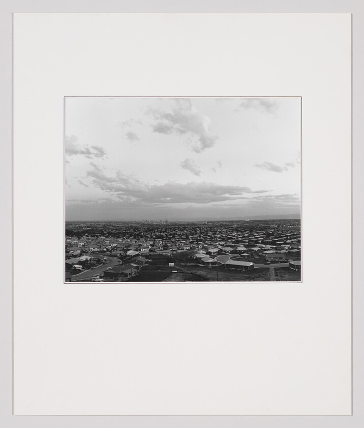 A black-and-white aerial view of a sprawling suburban neighborhood under a wide cloudy sky.