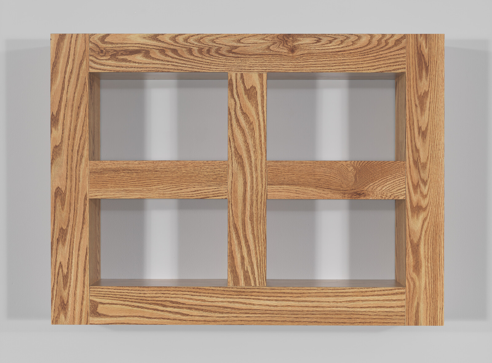 A wooden grid structure with nine square openings mounted on a white wall, casting soft shadows on the wall behind it. The wood has a prominent grain pattern, suggesting a strong natural texture.
