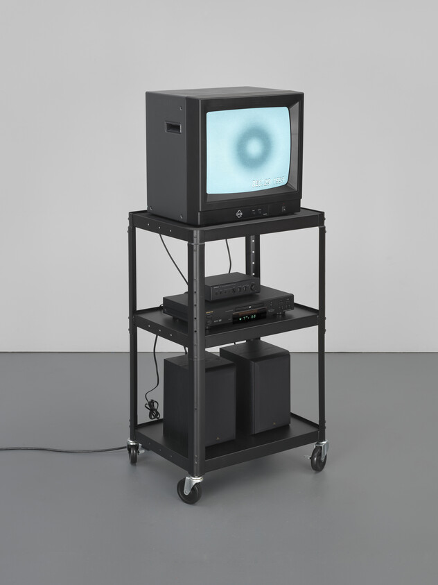 Old CRT television displaying a blue circular pattern on a black metal rolling cart with electronics.