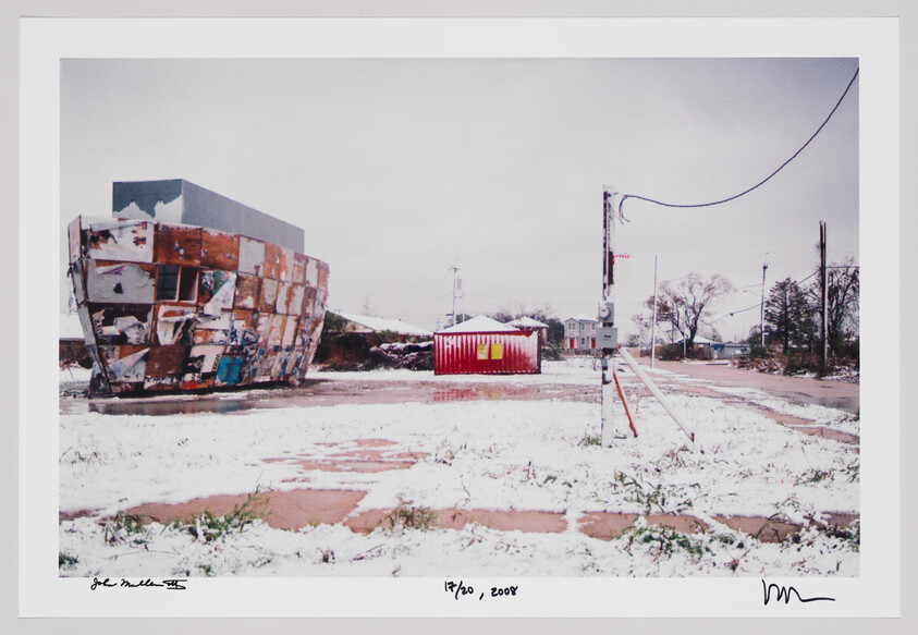 A snow-covered empty lot with a rusted patchwork metal structure and a red shipping container.