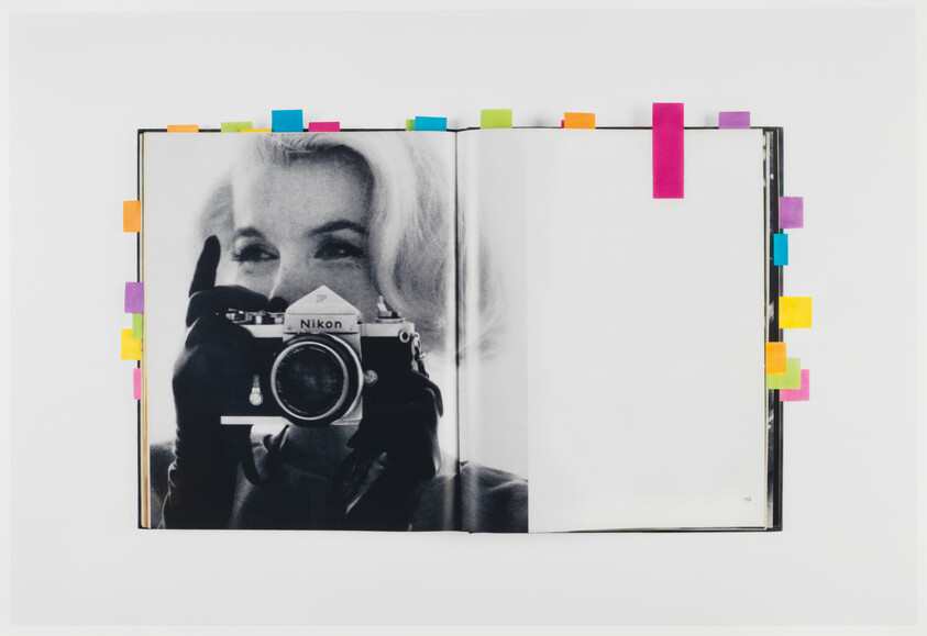 A book opened to a black-and-white photo of a woman holding a Nikon camera, with colorful sticky tabs.