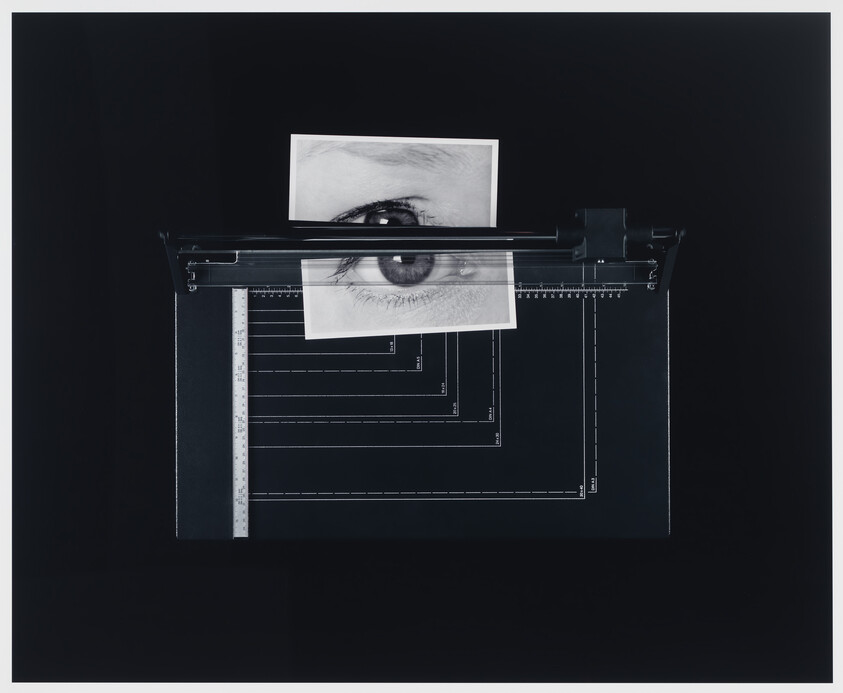A black and white photograph of a human eye is clipped to a drafting machine with a clear ruler and various technical drawing lines visible on a dark background.