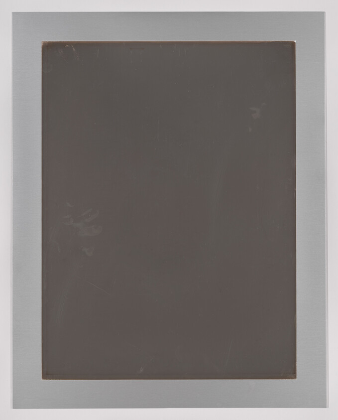 A photograph of a monochromatic dark square canvas framed with a light gray border, showing signs of wear and subtle marks on the surface.