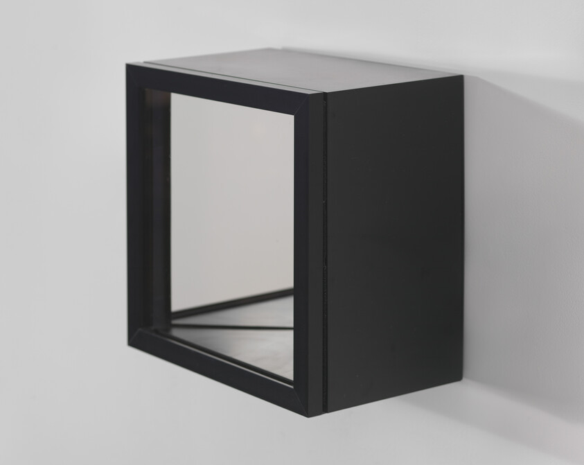 A black rectangular wall-mounted box with mirrored interior reflecting the room's corner.
