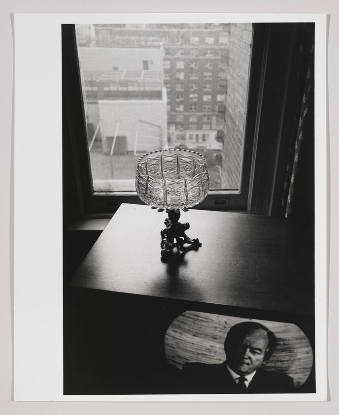 Cut-glass compote stands on a table by a window above a framed portrait of a man.