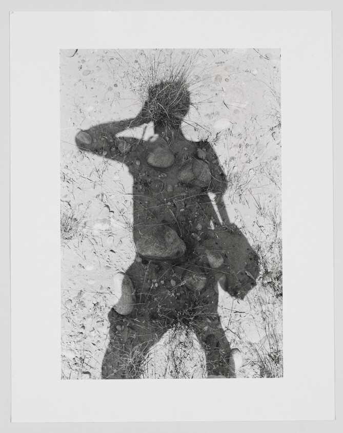 Shadow of a person holding a bag and shielding their eyes on rocky ground.