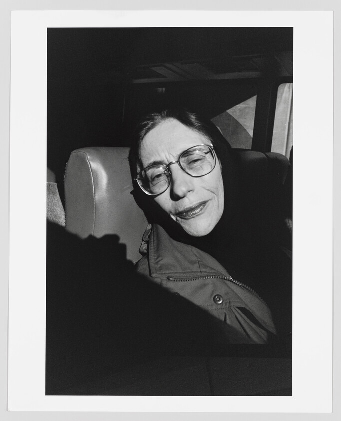 Older woman with glasses sits in a vehicle seat, eyes closed and smiling softly.