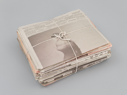 A bundled stack of newspapers tied with white string resting on a light gray surface.