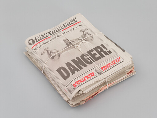 Stack of newspapers tied with string showing a front-page headline reading "DANGER!".