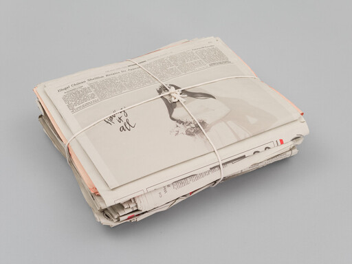 A bundle of newspapers and pages tied together with white string on a gray surface.