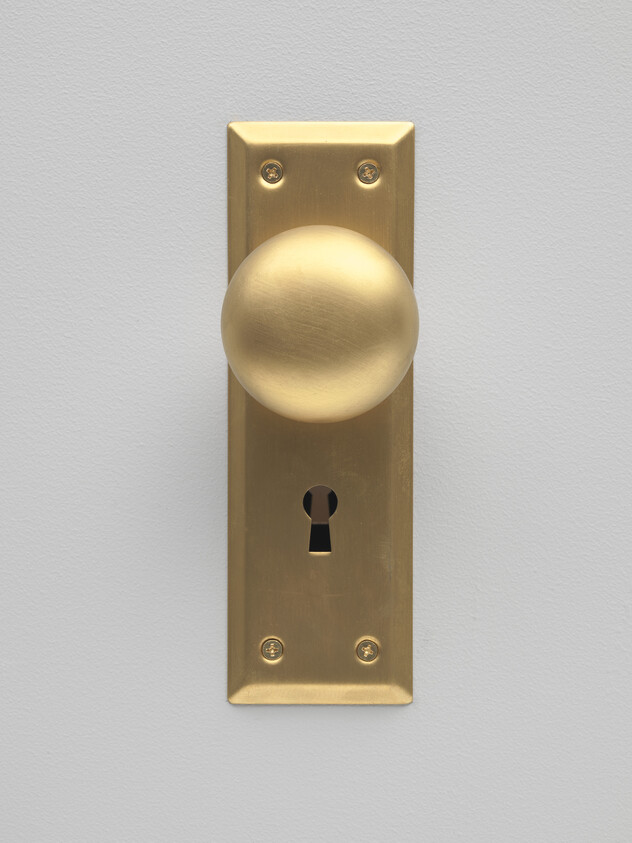 Brass round doorknob on a rectangular backplate with a keyhole mounted on a gray door.
