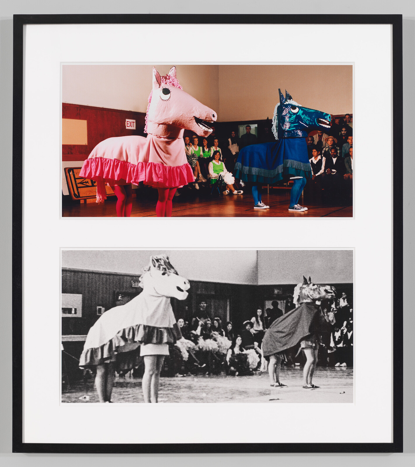 Two performers in oversized pink and blue horse costumes dance in a gymnasium in front of a seated audience.
