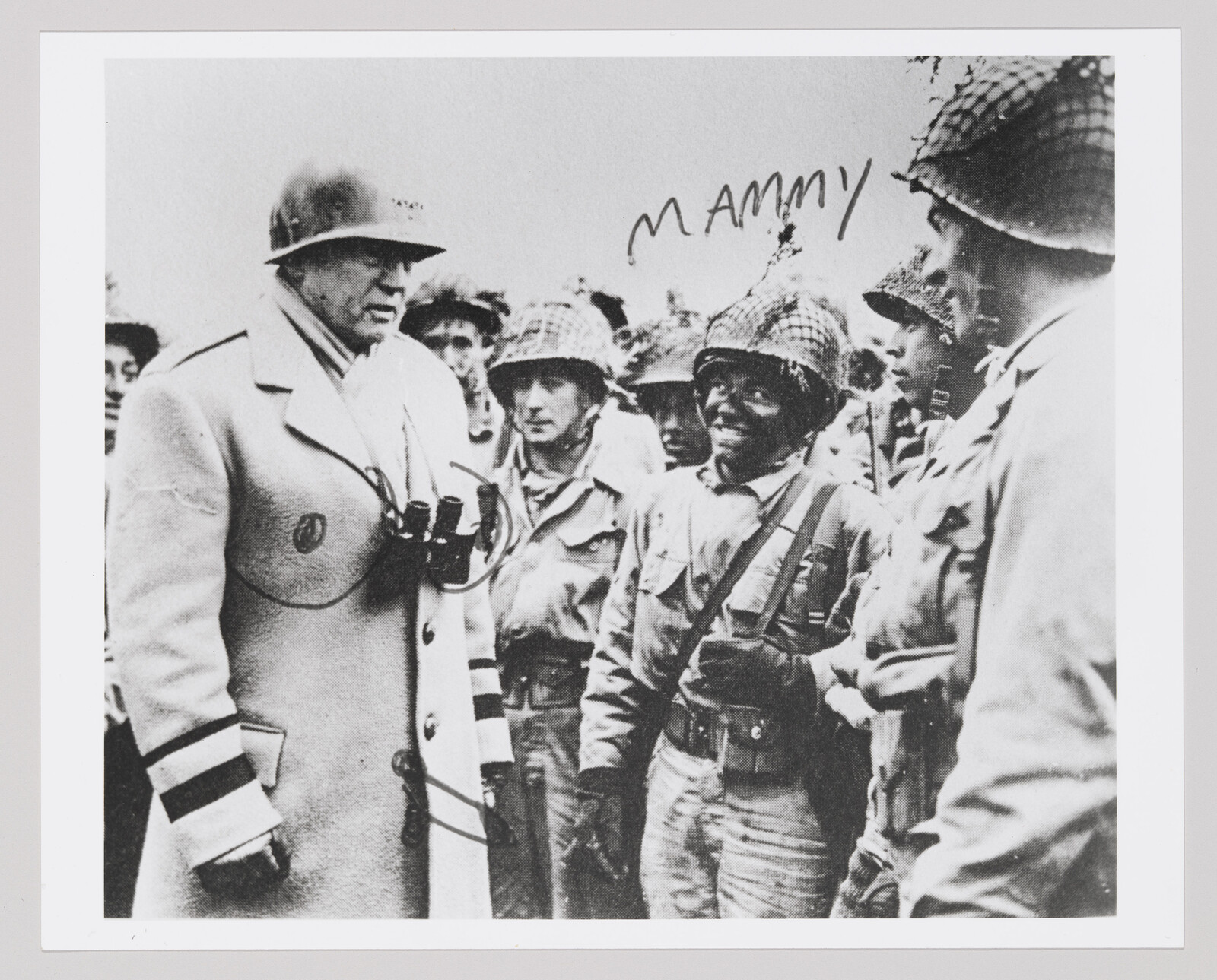 An officer wearing a long coat and helmet speaks with a group of soldiers in helmets.