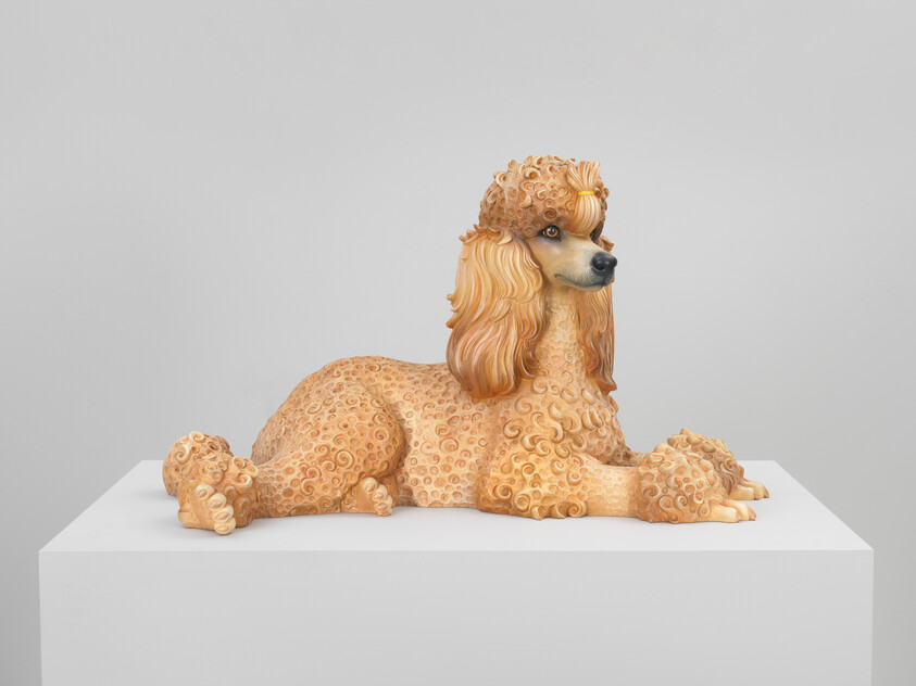A highly detailed sculpture of a poodle with an elaborate and stylized coat featuring intricate curls and patterns, displayed on a white pedestal against a neutral background.