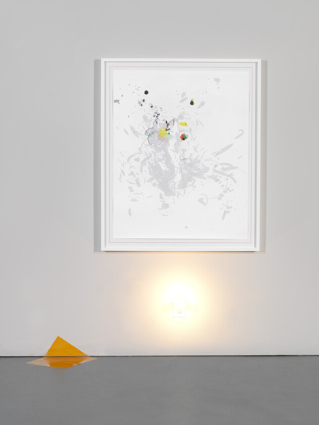 Framed abstract painting hangs above a glowing night light and a folded orange paper on the floor.