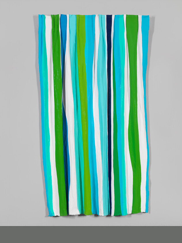 A vertically striped curtain in shades of blue, green, and white hanging against a gray wall.