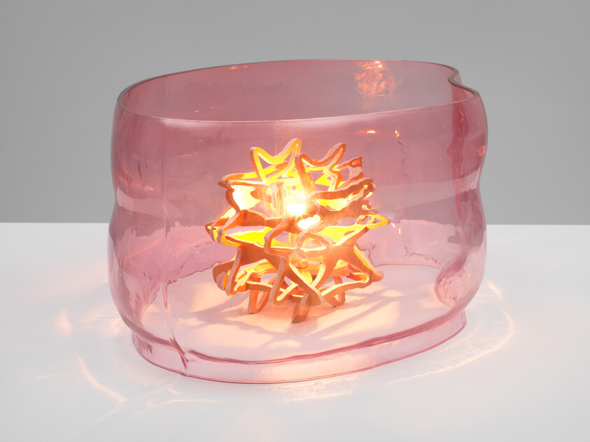 A glowing star-shaped wooden sculpture sits inside a translucent pink glass bowl, casting warm reflections.