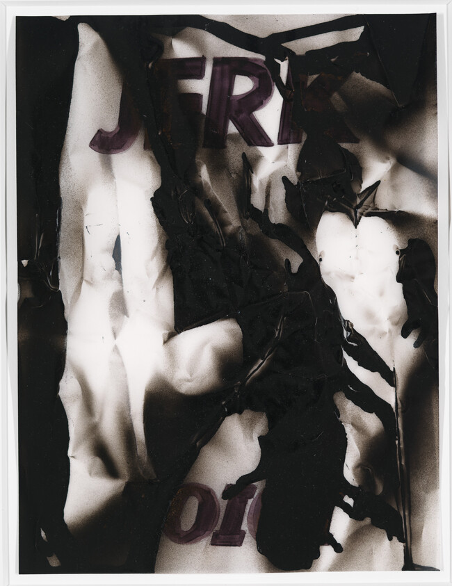 Crumpled, burnt black-and-white paper with partially visible purple letters and charred edges.