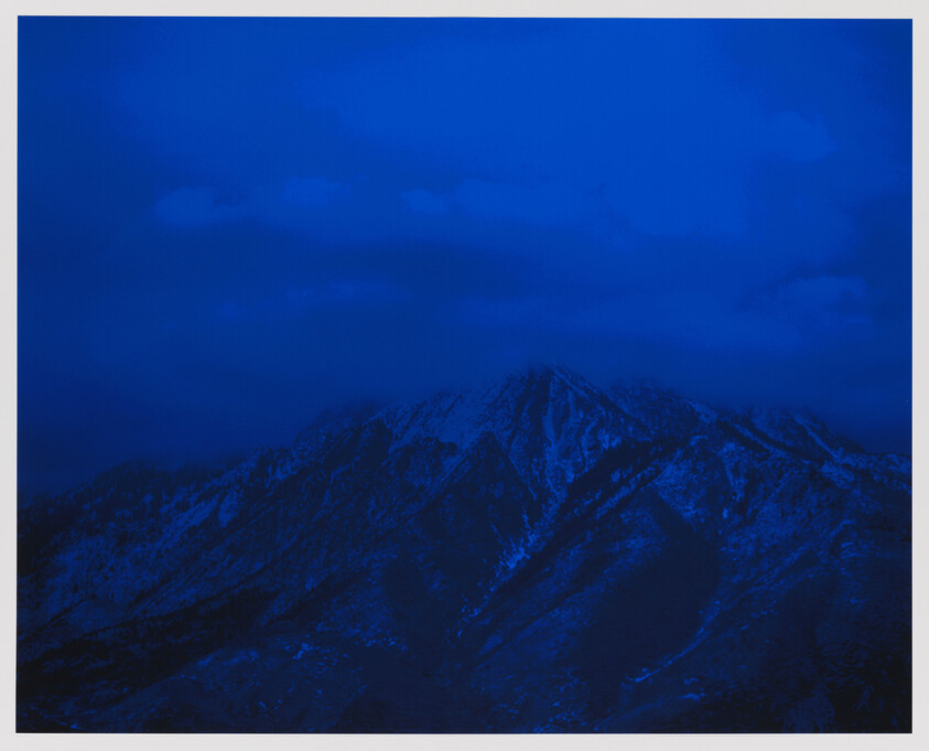 Snow-dusted mountain peaks loom under a deep blue evening sky.