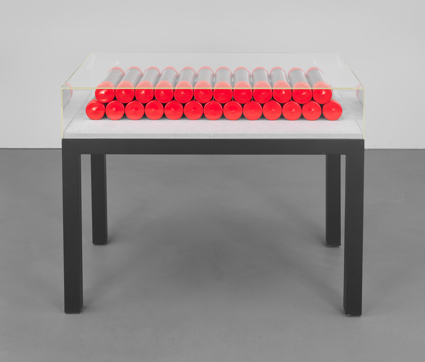A glass display on a table holds three orderly rows of bright red cylindrical objects.