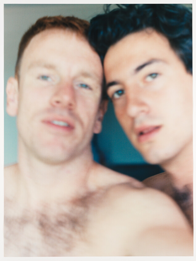 Two shirtless men stand closely together looking at the camera in a blurred, intimate selfie.