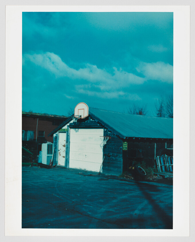 A weathered garage with a basketball hoop above the closed door beside a cracked driveway.
