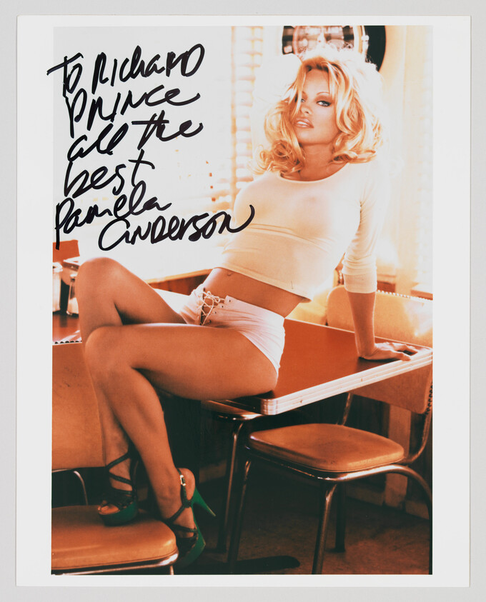 Blonde woman in a white crop top and shorts posing on a diner table with a large handwritten dedication.