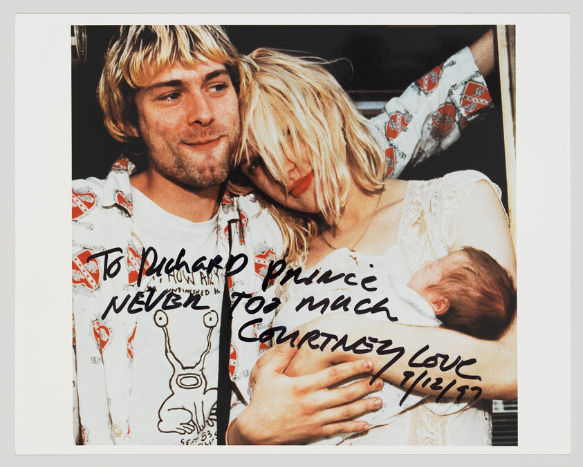 A smiling man and woman hold a newborn while the woman leans her head on his shoulder.