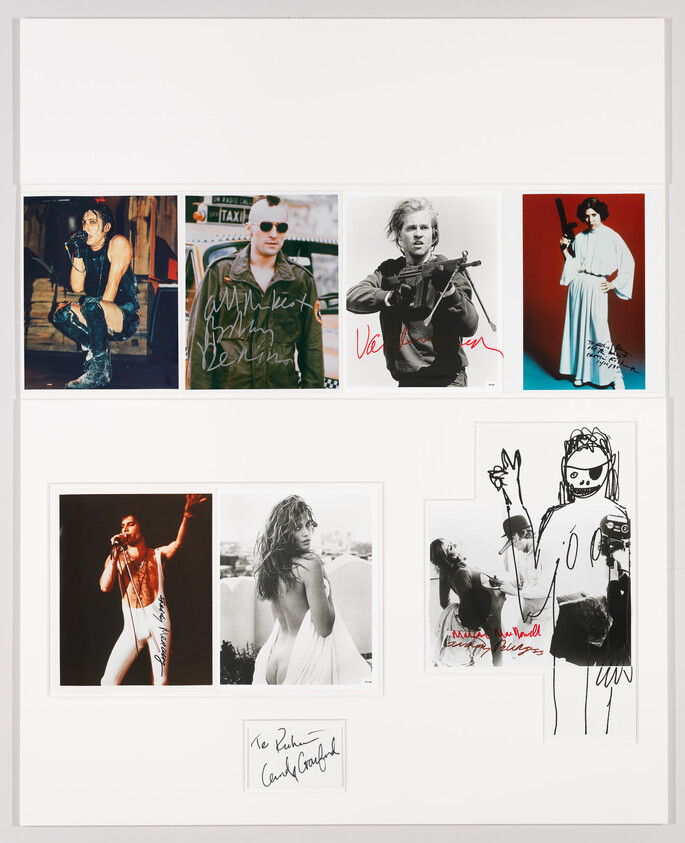 A framed collage of signed celebrity photographs and sketches arranged in a white mat.