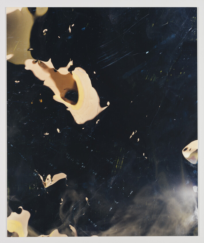 Dark glossy surface with scattered cream and yellow paint-like splashes and small reflective specks.