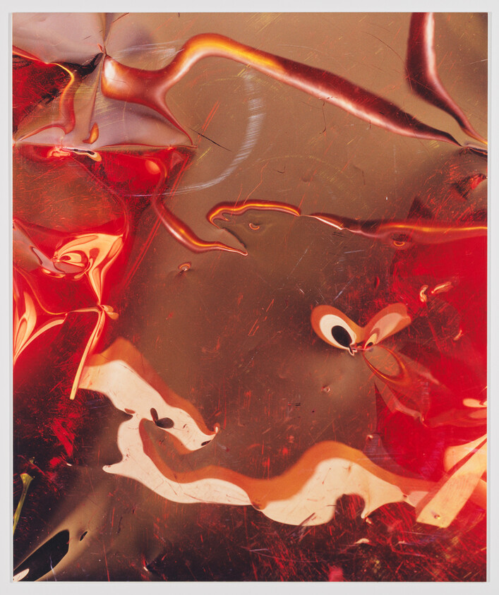 Shiny red and gold distorted plastic sheet with twisting reflections and fluid shapes.
