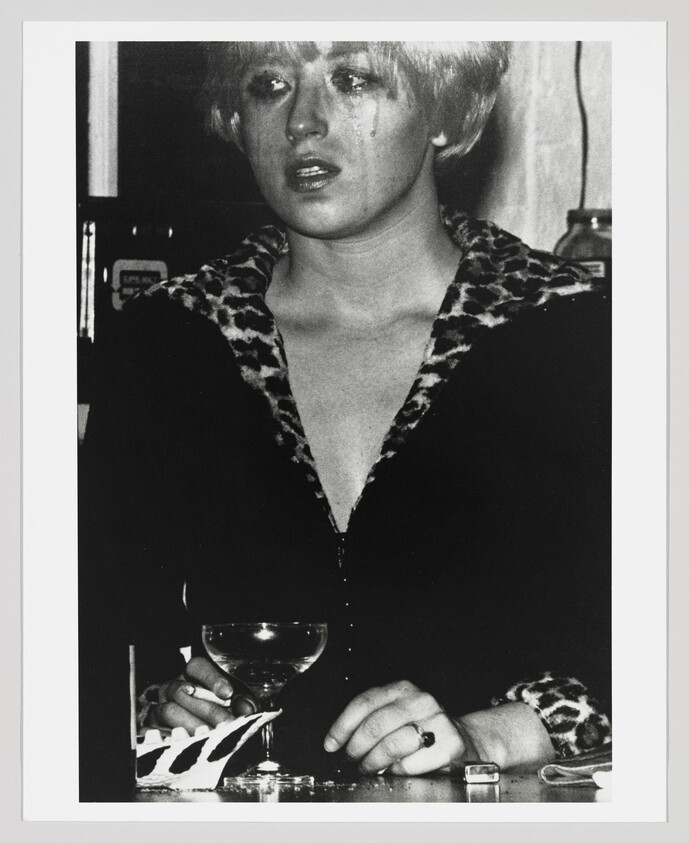 Young woman with smeared makeup holds a cocktail glass at a bar, looking distressed.