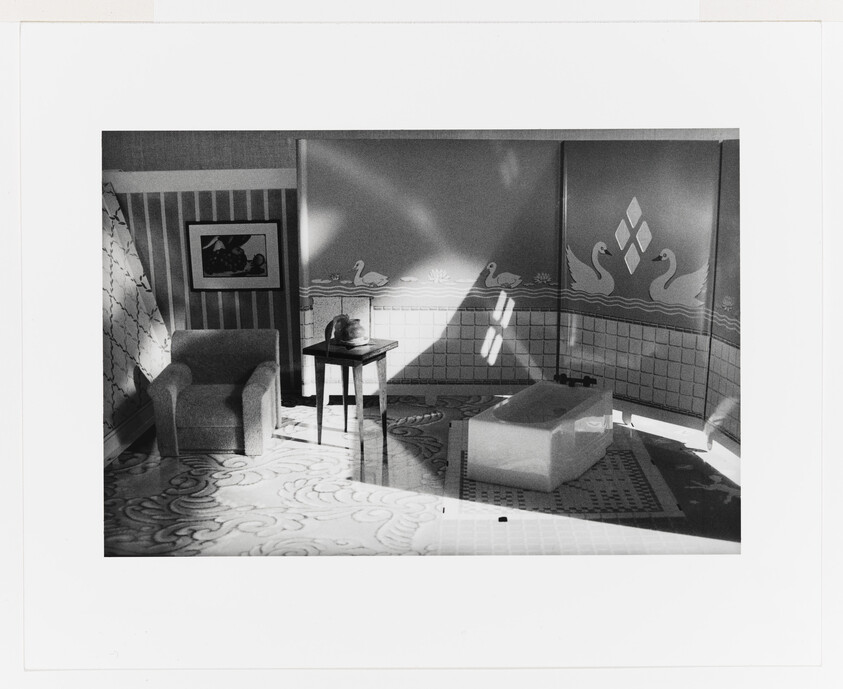 A sunlit bathroom set with a freestanding bathtub, armchair, small table, and swan wall mural.