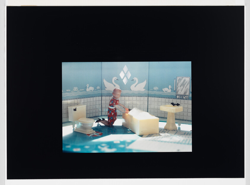 A child doll kneels by a bathtub filling with bubbles in a blue swan-themed bathroom.
