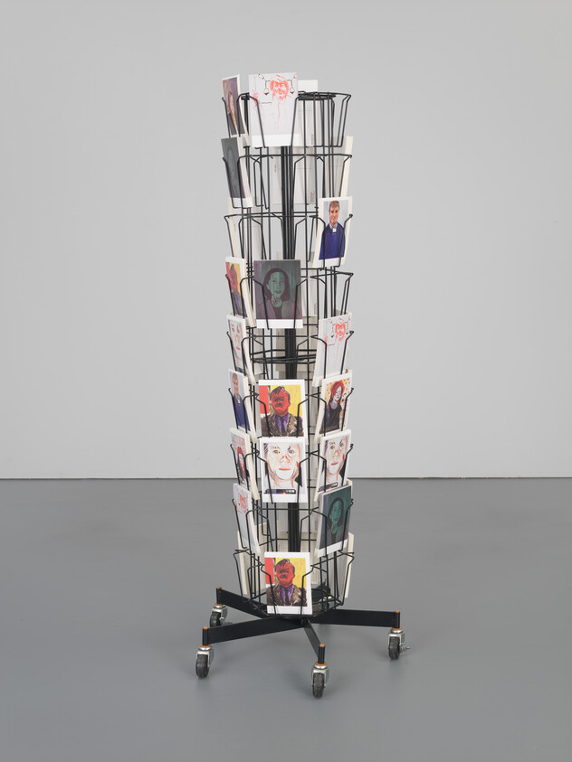 Tall rotating metal rack on wheels holding multiple portrait postcards in wire display slots.