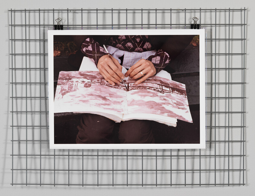 A person paints a watercolor landscape in a sketchbook while holding a paintbrush over the page.