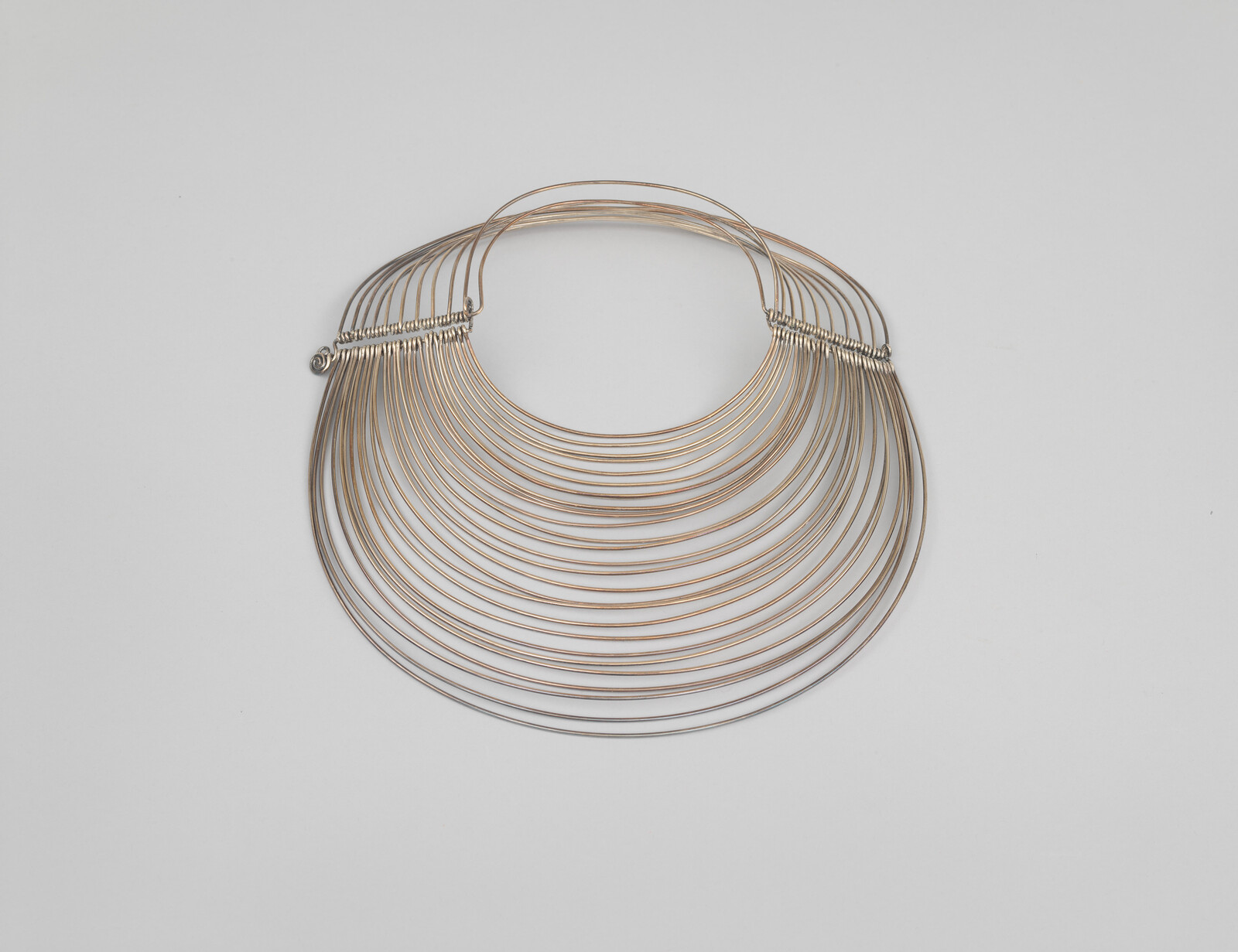 Thin gold wire collar necklace made of many graduated concentric loops resting on a white background.