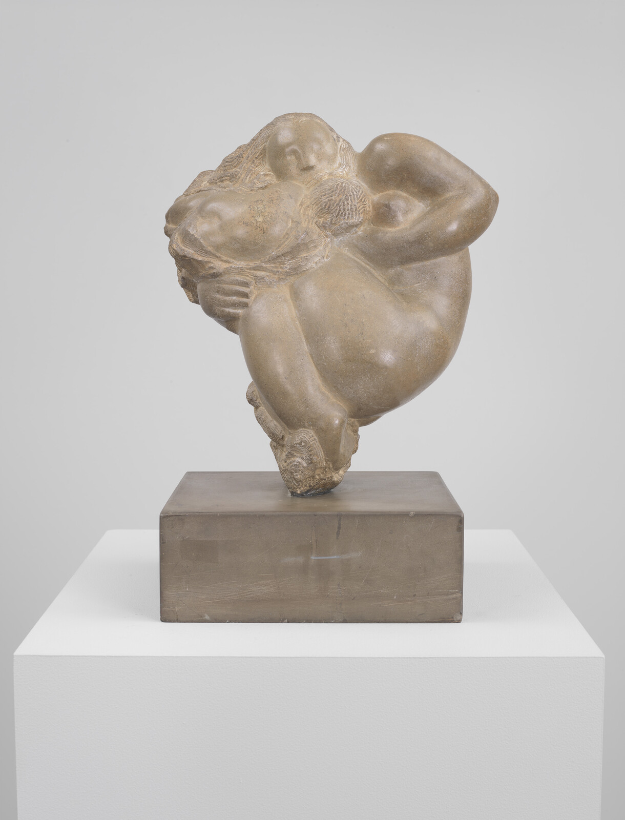 Bronze sculpture of two intertwined figures curled together in a close embrace on a pedestal.