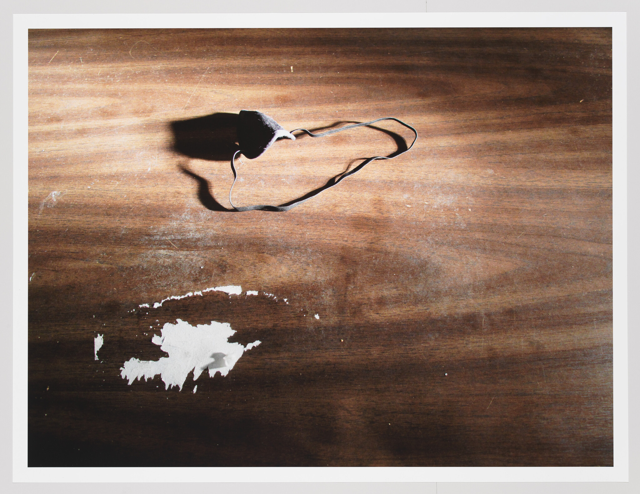 A black cloth face mask with elastic strap lies on a worn wooden table with peeling white paint.