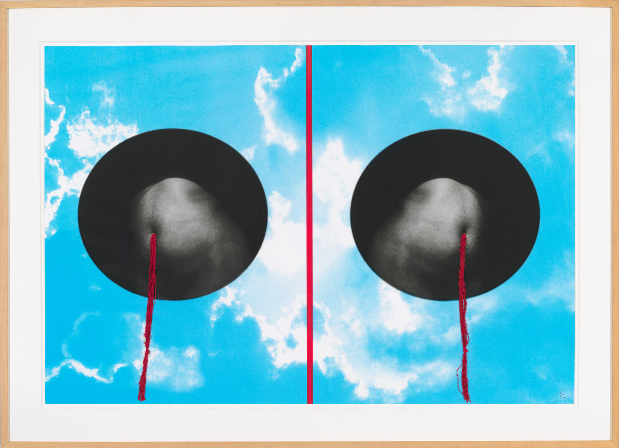 Two black circular hats against a bright blue sky with red tassels hanging down.