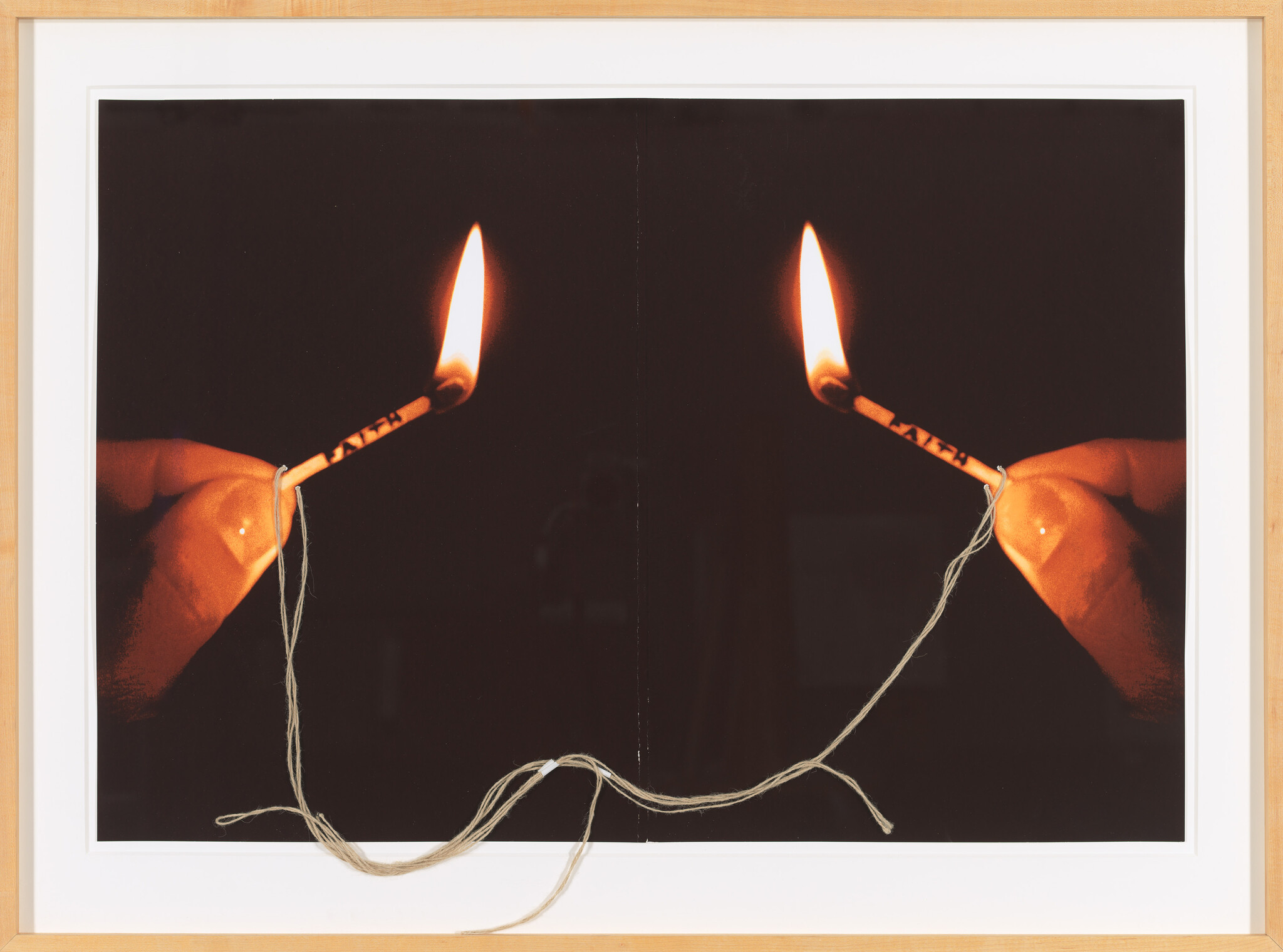 Two lit matches held by hands burning at each end of a tied string between them.