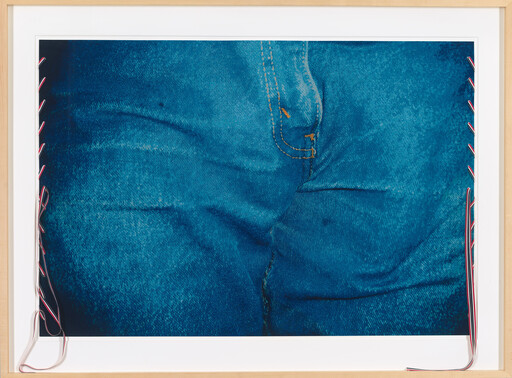 Close-up of blue denim jeans with stitched seam and decorative ribbons tied along the frame.