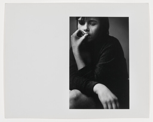 A young person sits pensively, resting chin on hand and touching their lips in a black-and-white portrait.
