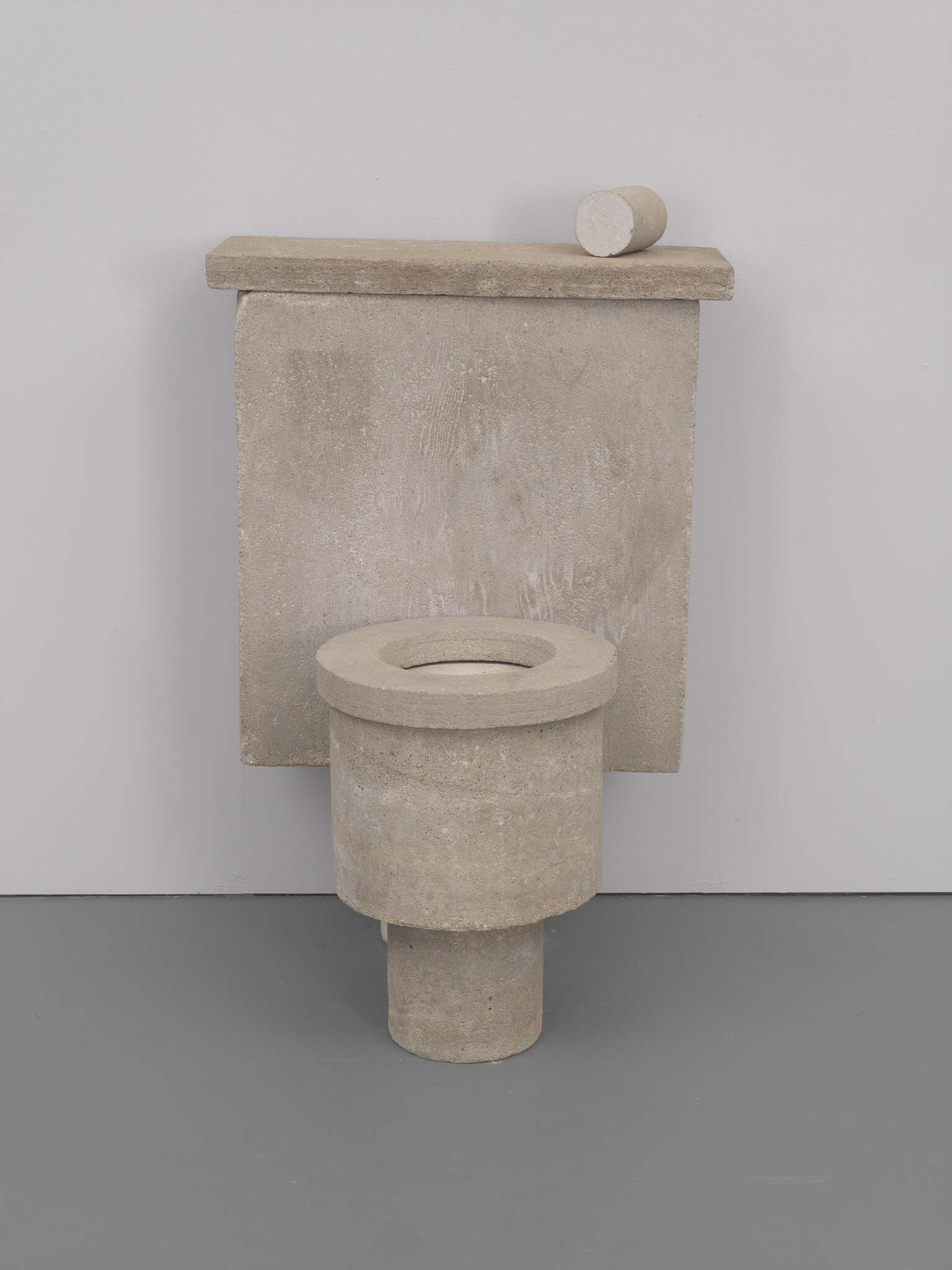 A toilet made entirely of rough, gray stone with a matching cylindrical stone piece resting on top.