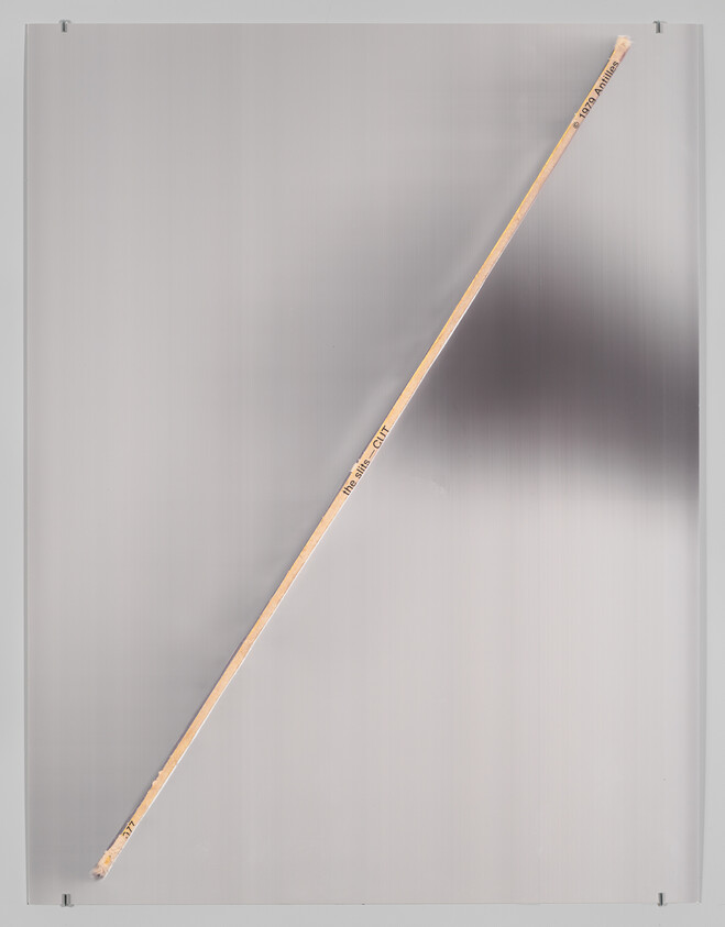 A long wooden dowel placed diagonally across a smooth silver metal surface.