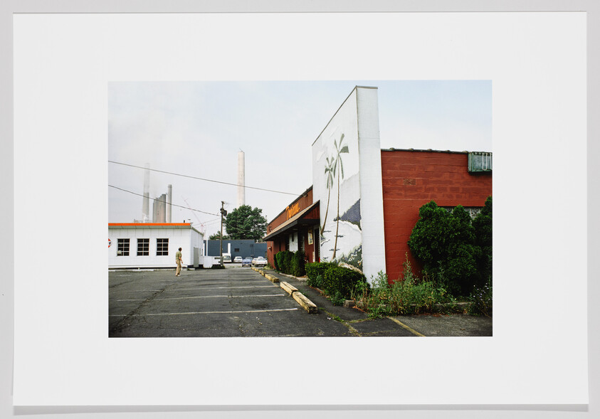 Empty parking lot beside a red brick building with a palm mural and a lone person walking.