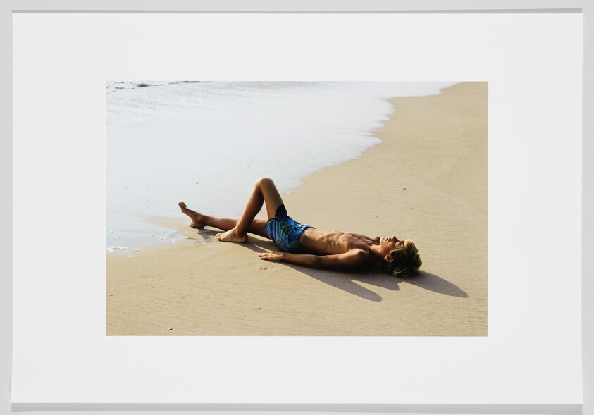 A young man lies on wet sand near the shoreline, relaxing and soaking up the sun.