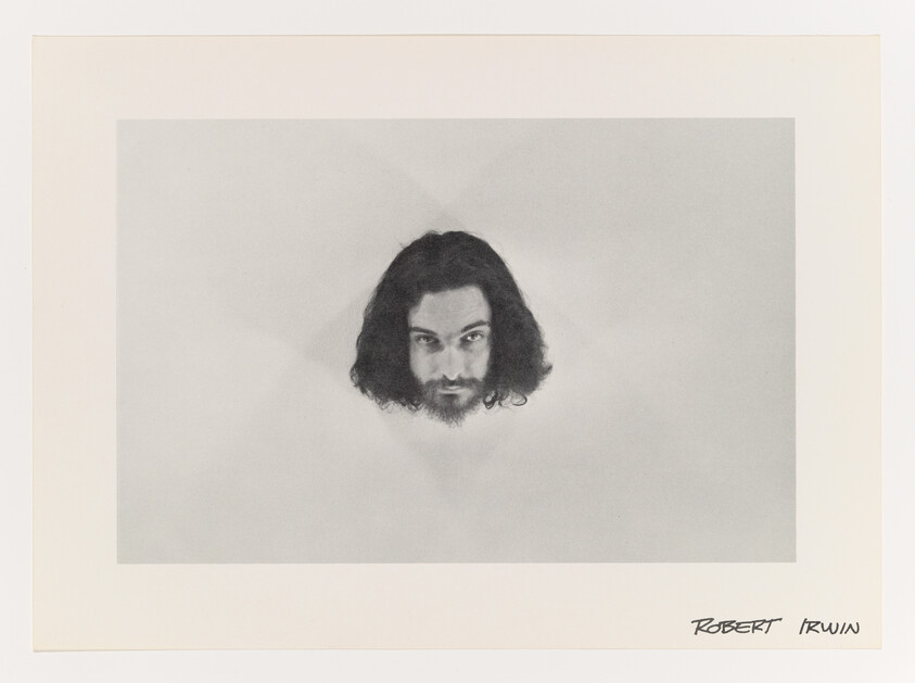 A bearded man’s floating head with long hair centered on a pale background.